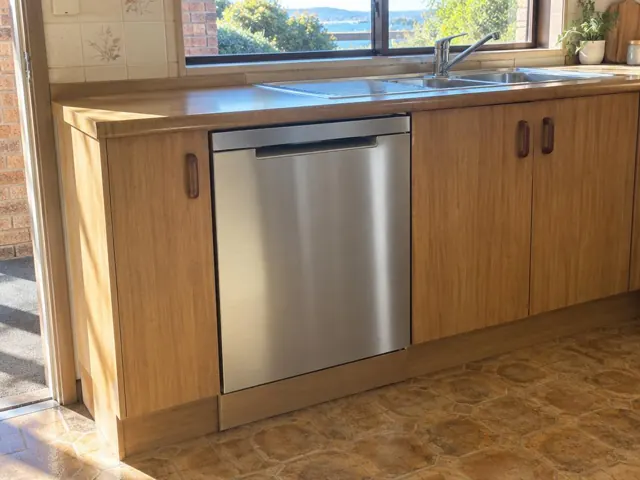 Stainless dishwasher built into a timber kitchen under a benchtop beside a sink in Fennell Bay