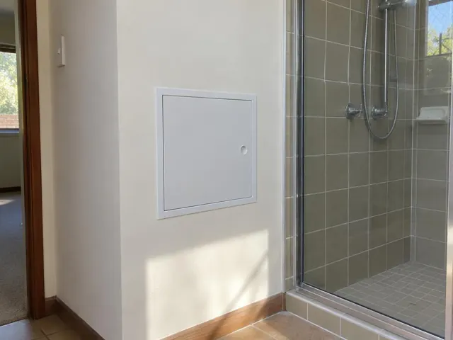 Neat access panel in a painted bathroom wall beside a tiled shower in Woodrising